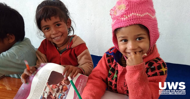 Two children sitting at a table with educational materials, smiling. With UWS logo, educate the future, change the future.